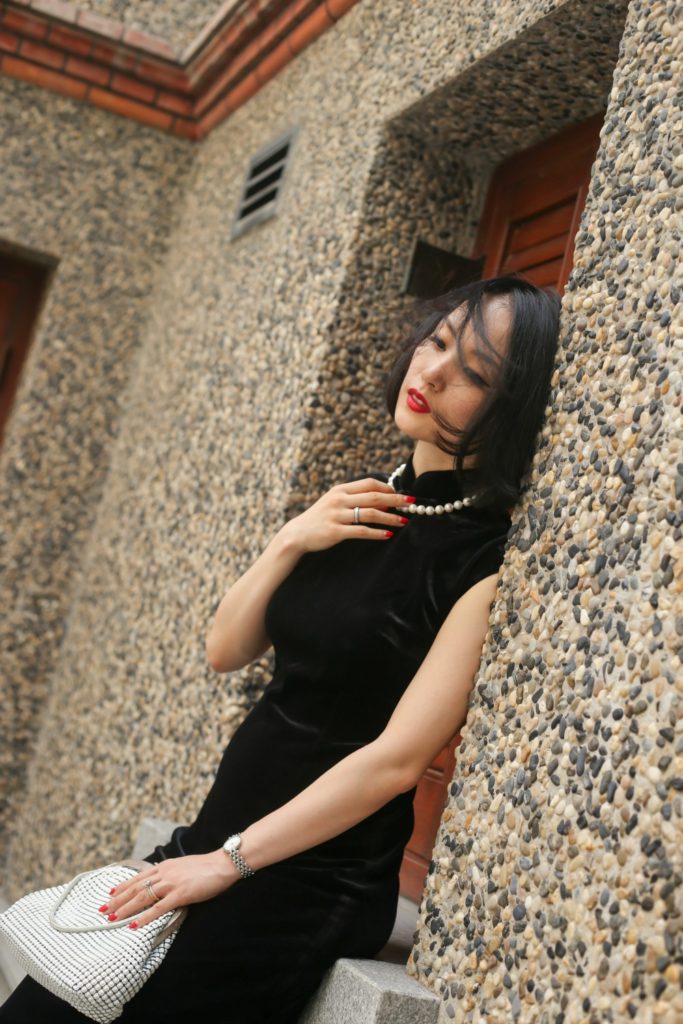 Miranda wearing black sleeveless velvet qipao Sinan Mansions leaning against wall